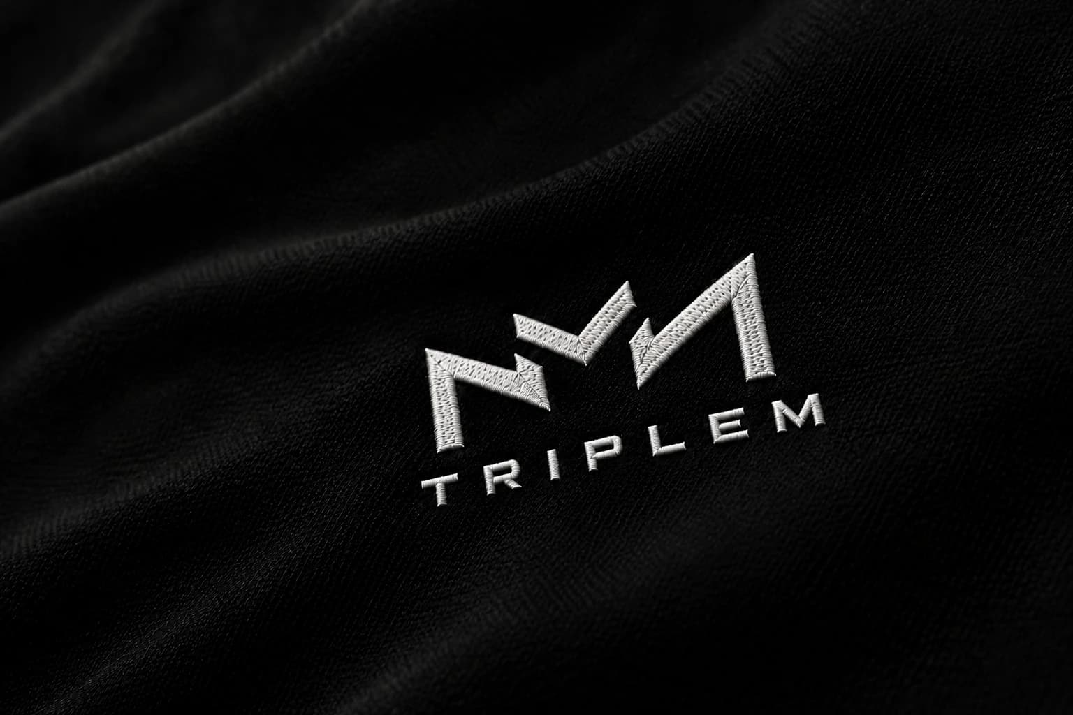 نمای نزدیک گلدوزی نشان TRIPLEM روی پارچه مشکی
